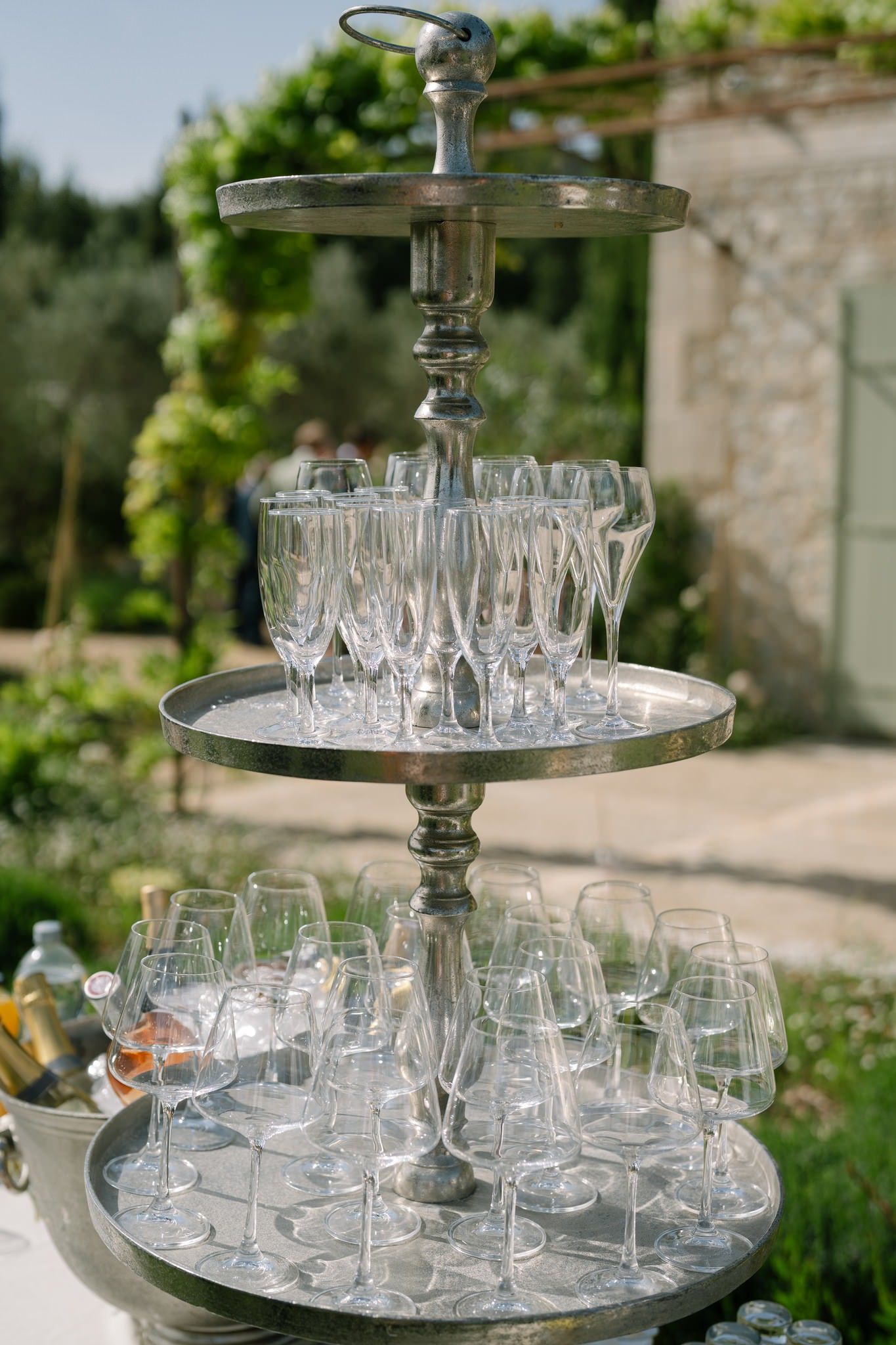 Tiered glass display stand holding crystal champagne glasses at an outdoor event.