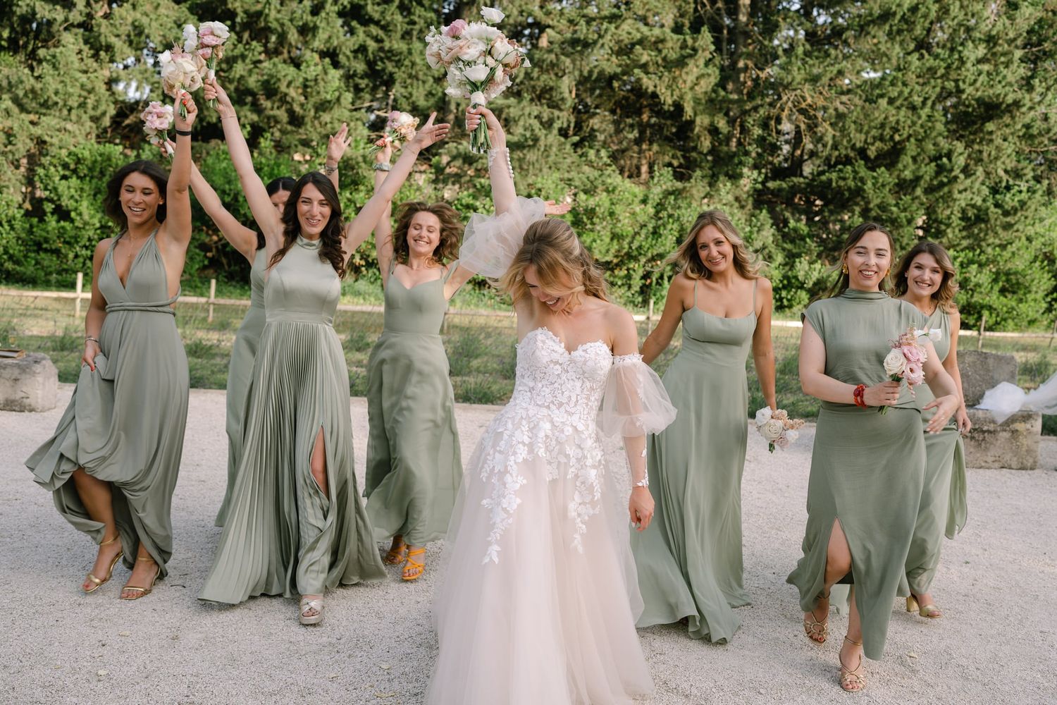 Joyful wedding party celebrating on a stone path surrounded by greenery.
