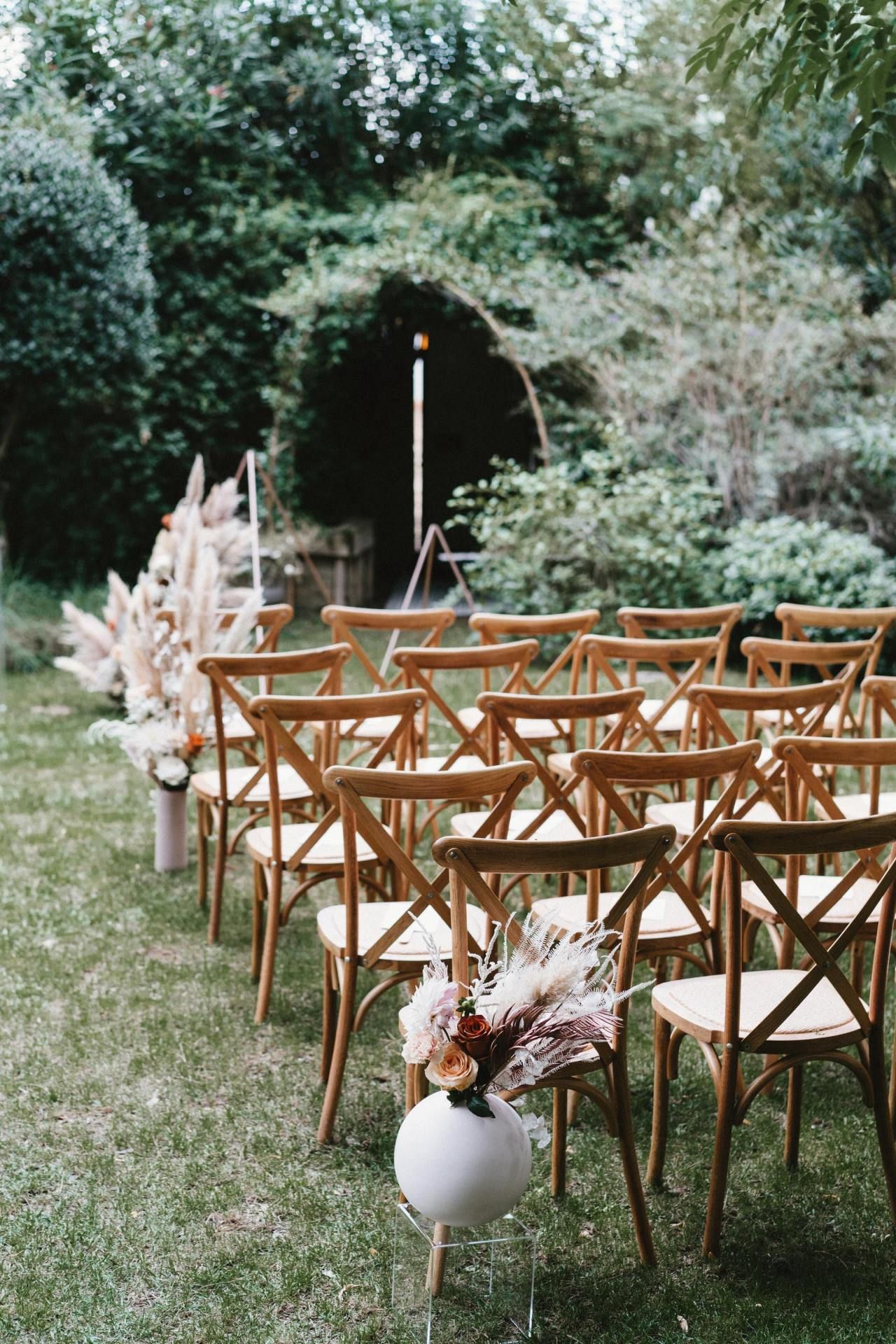 Wooden chairs arranged in rows for an outdoor wedding ceremony with floral decorations.