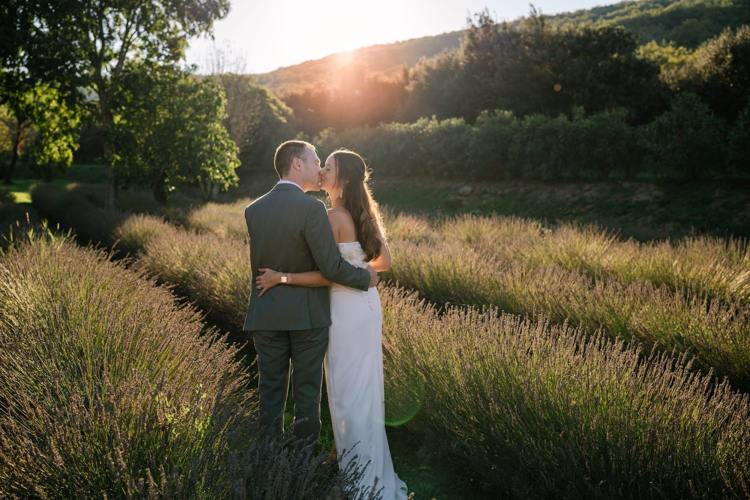 Newlyweds walking through tall grass during sunset.