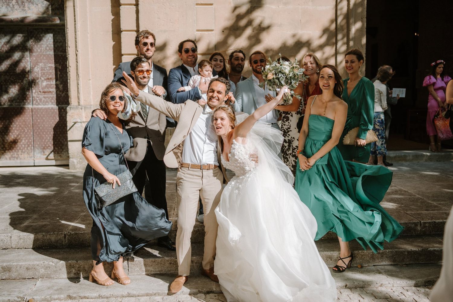 Wedding party celebrates joyfully on stone steps of a historic building in elegant attire.