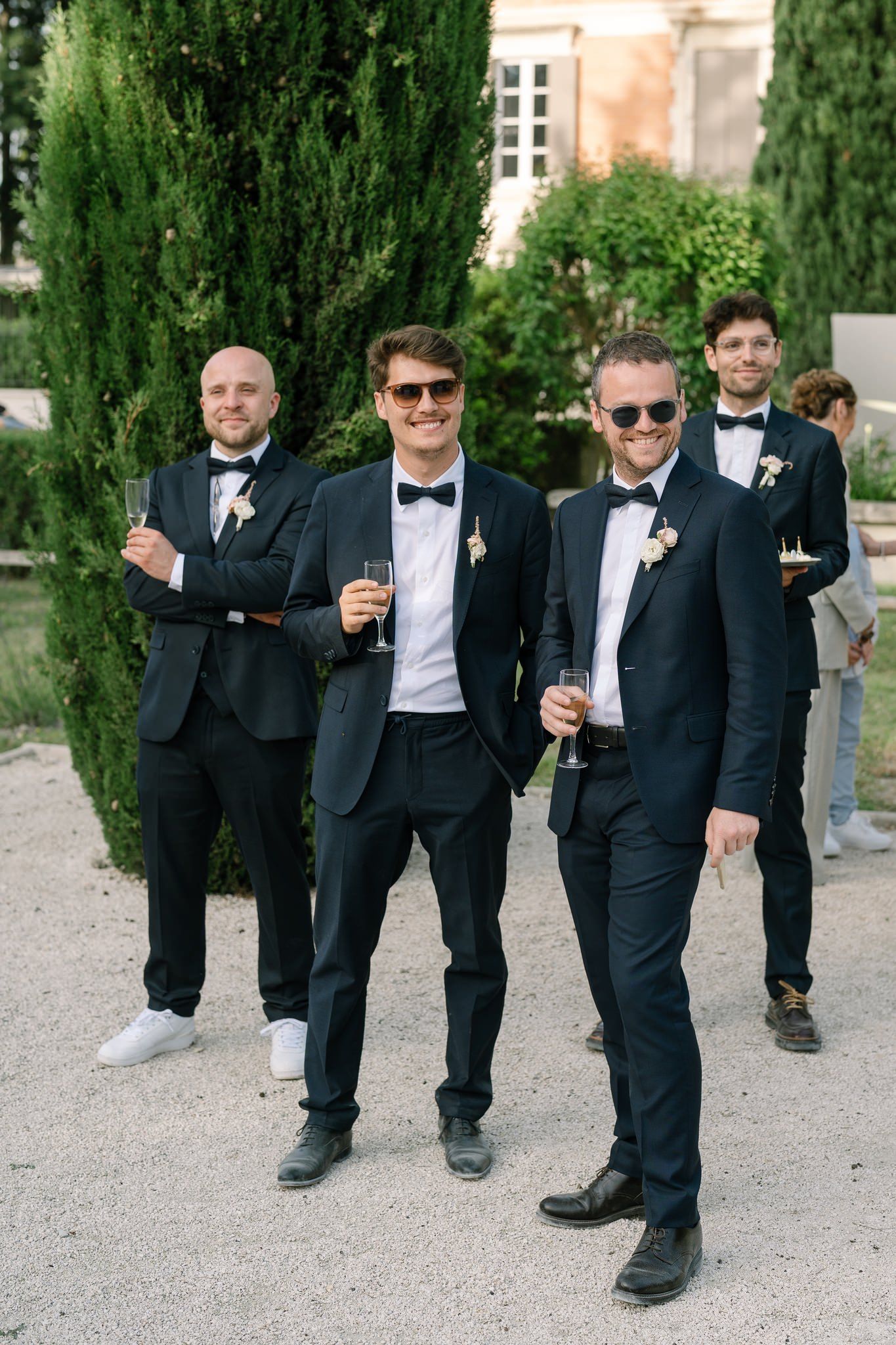 Group wearing formal black tuxedos walking together on a garden path.