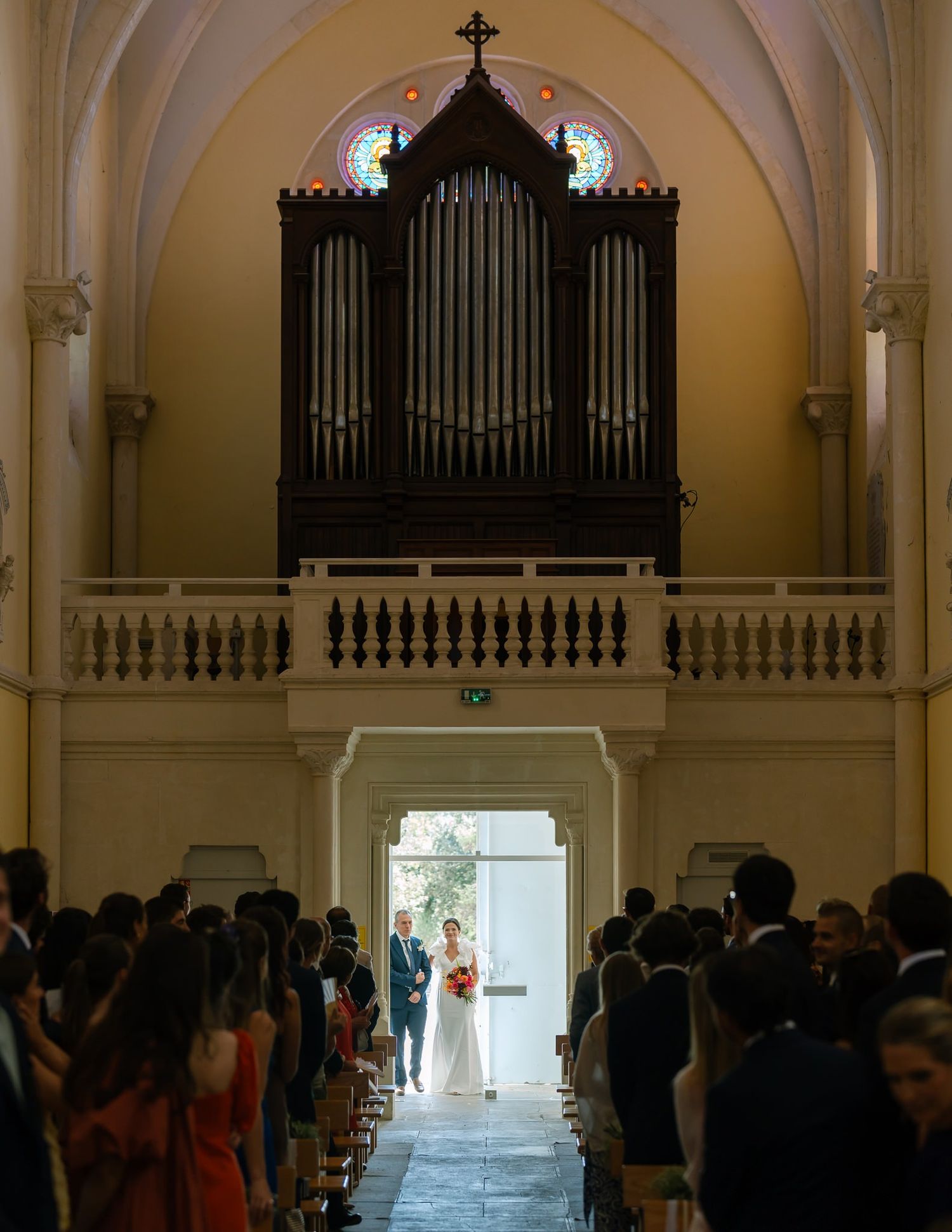 A grand pipe organ sits above wedding guests in a traditional church sanctuary during a ceremony.