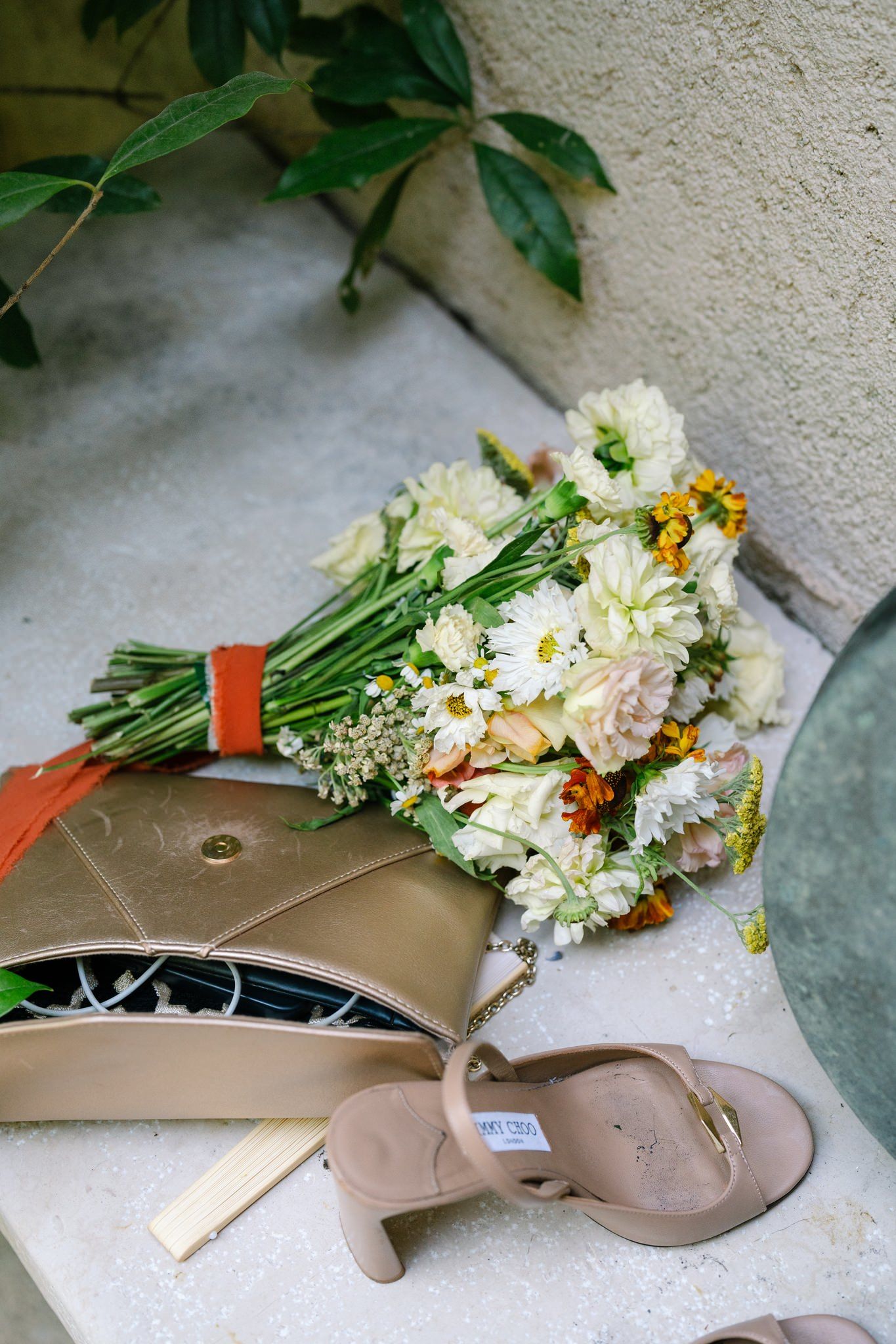 Wedding shoes and floral bouquet arranged on a beige surface.