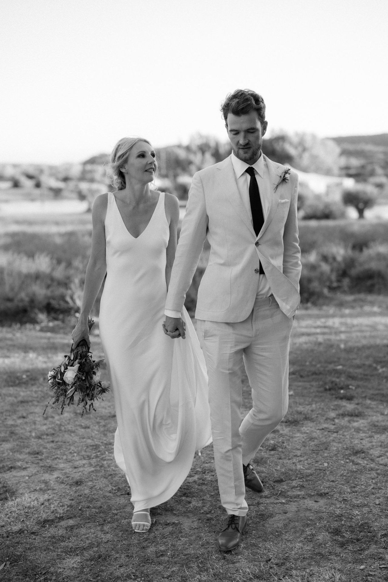 Wedding couple running through a field in all-white attire captured in black and white photography.