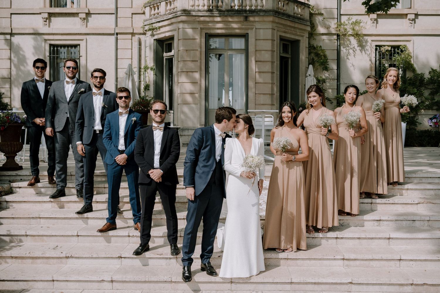 Wedding party lined up on grand stone steps with bridesmaids in champagne dresses.