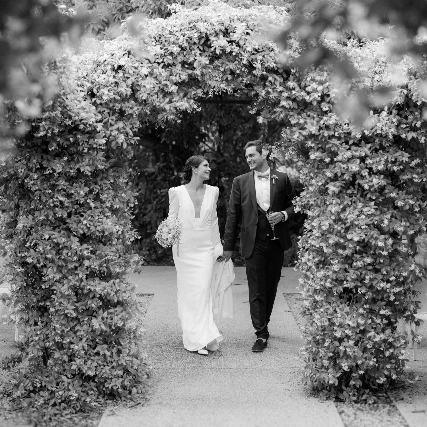 Couple walking through garden archway with blooming flowers.