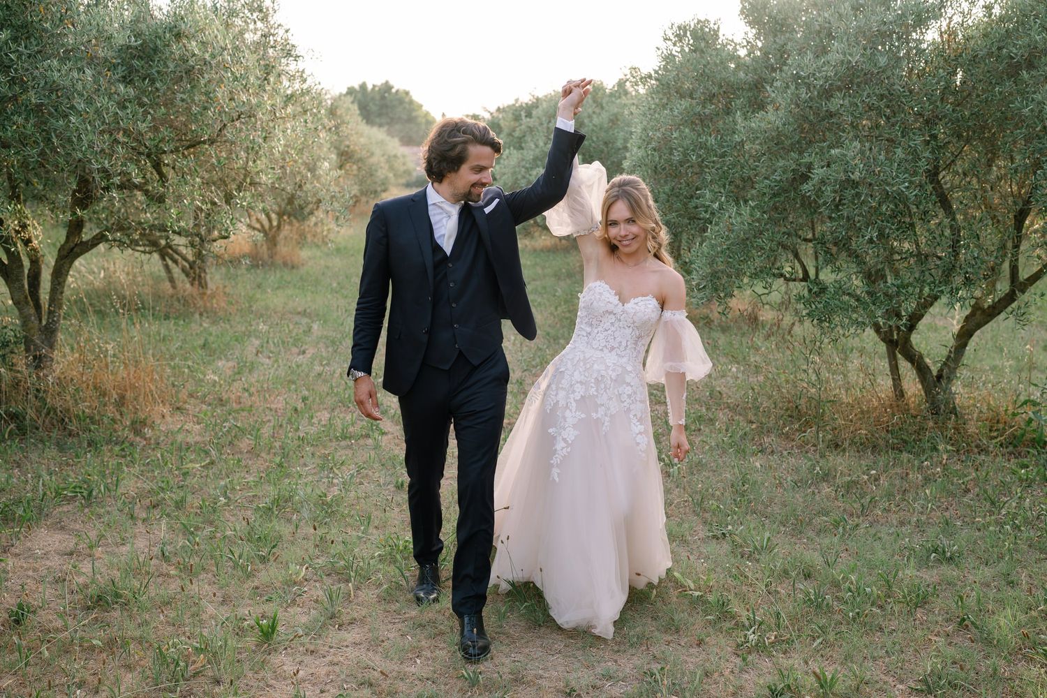 Newlyweds walk hand in hand through a sunlit Mediterranean garden.