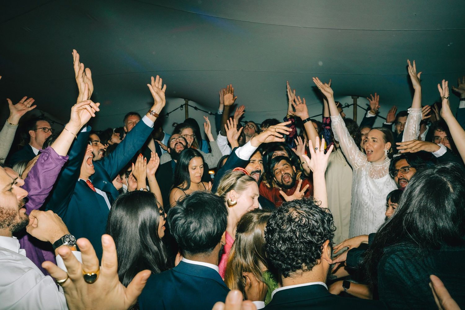 Energetic crowd with raised hands dancing and celebrating at a lively party reception.