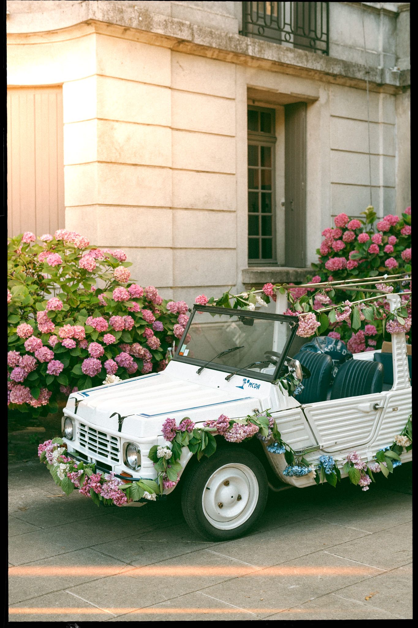 White vintage Citroen decorated with pink roses parked in front of a French building.