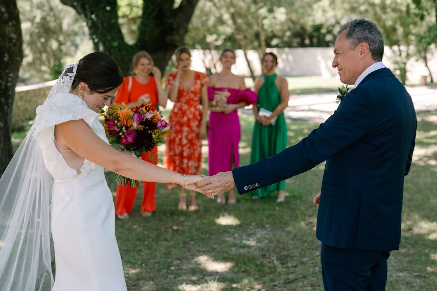 Outdoor wedding celebration with guests in colorful attire under tree canopy.