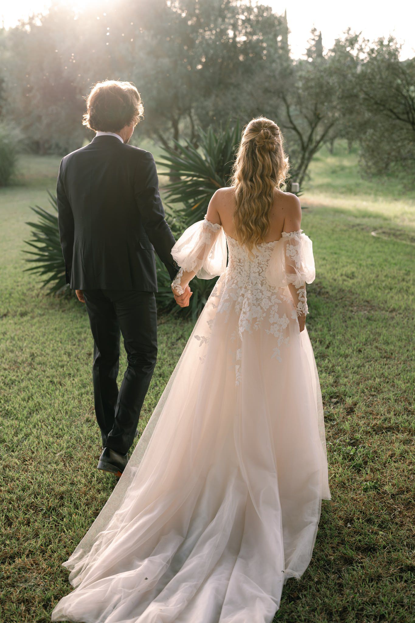 Couple walking through a sunlit garden in formal wedding attire.