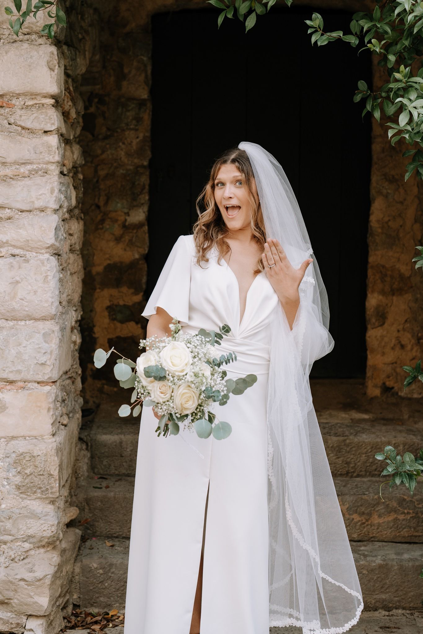 Elegant bridal portrait in a stone archway featuring a white wedding gown and flowing veil.