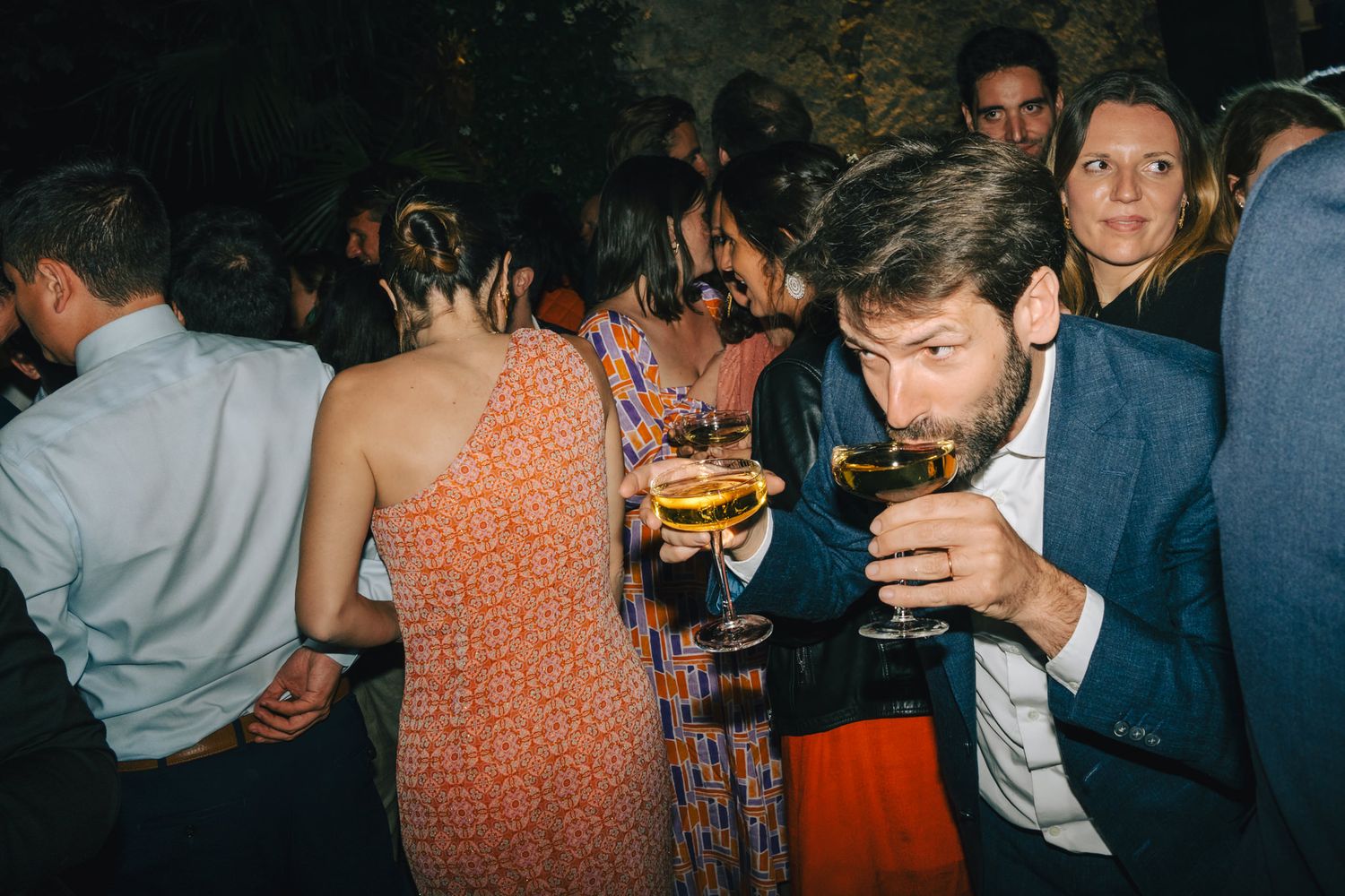 Party guests mingling and enjoying drinks at a dimly lit social gathering.