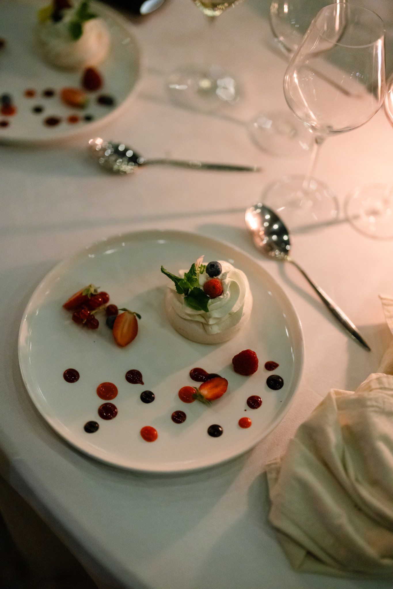 Elegant plated desserts with artistic sauce dots on white tablecloth at wedding reception.