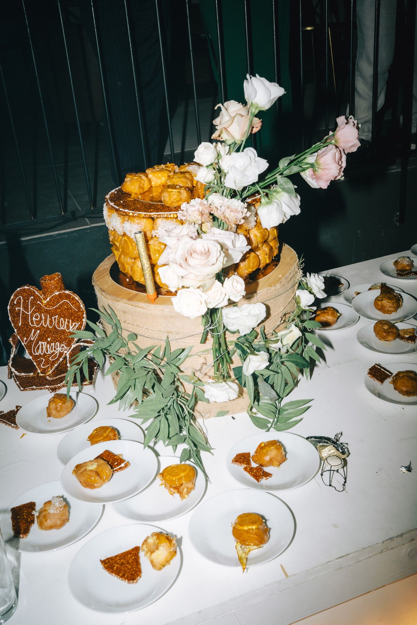 Elegant wedding cake display with pink roses and greenery on white tablecloth.