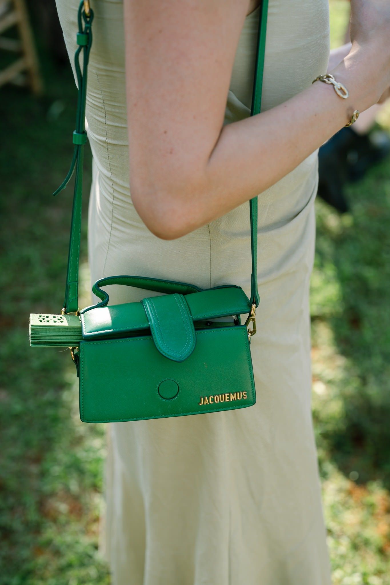 Close-up of a green leather crossbody bag against a light-colored dress.