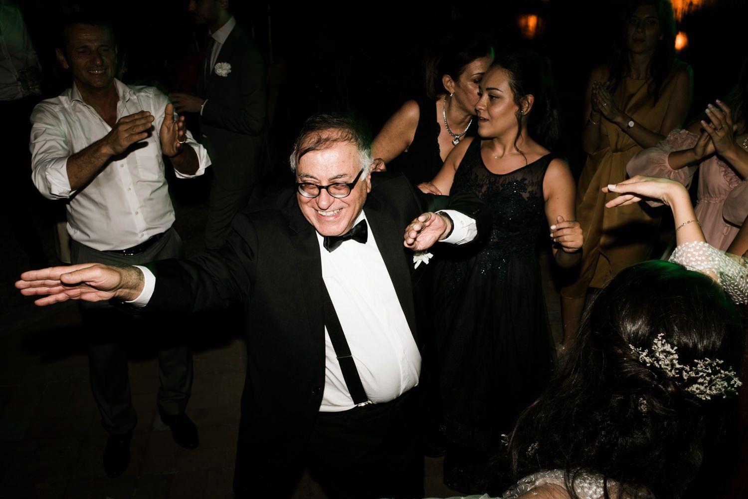 Partygoers dancing enthusiastically in formal attire at a nighttime celebration.