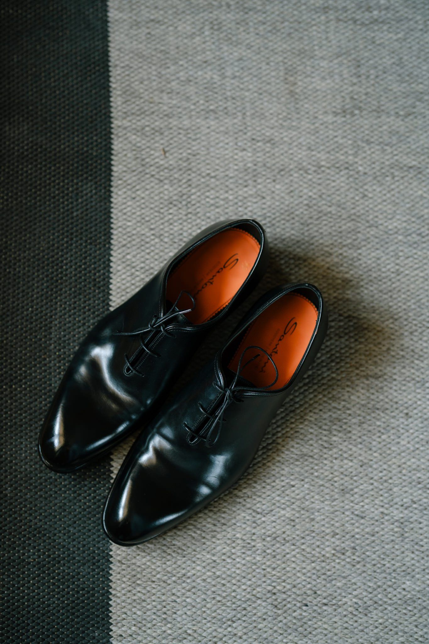 Shiny black leather dress shoes displayed on gray carpet.