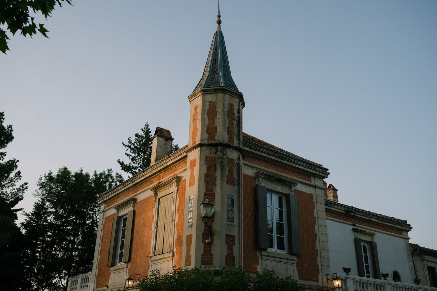Historic brick building with a pointed tower and ornate architecture at sunset.