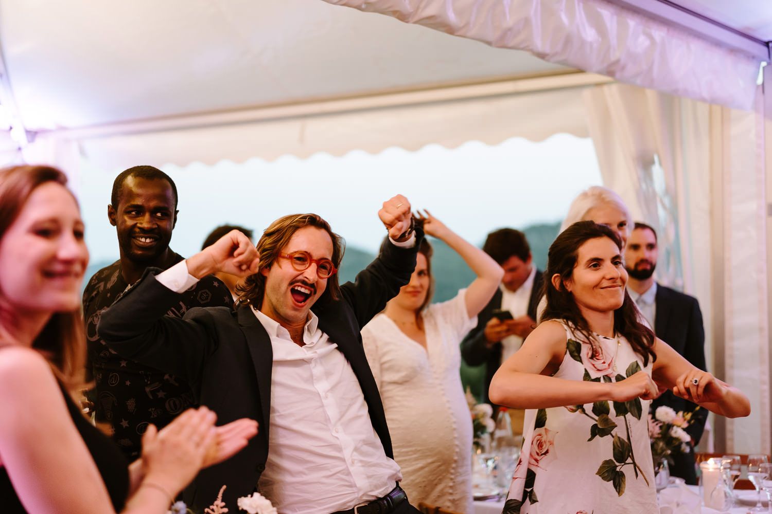 Wedding reception guests dancing and celebrating under a white tent.
