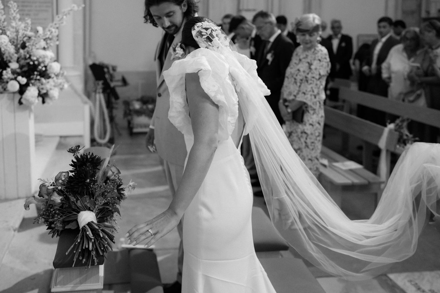 An elegant bride in a fitted white gown with flowing veil stands in a church.