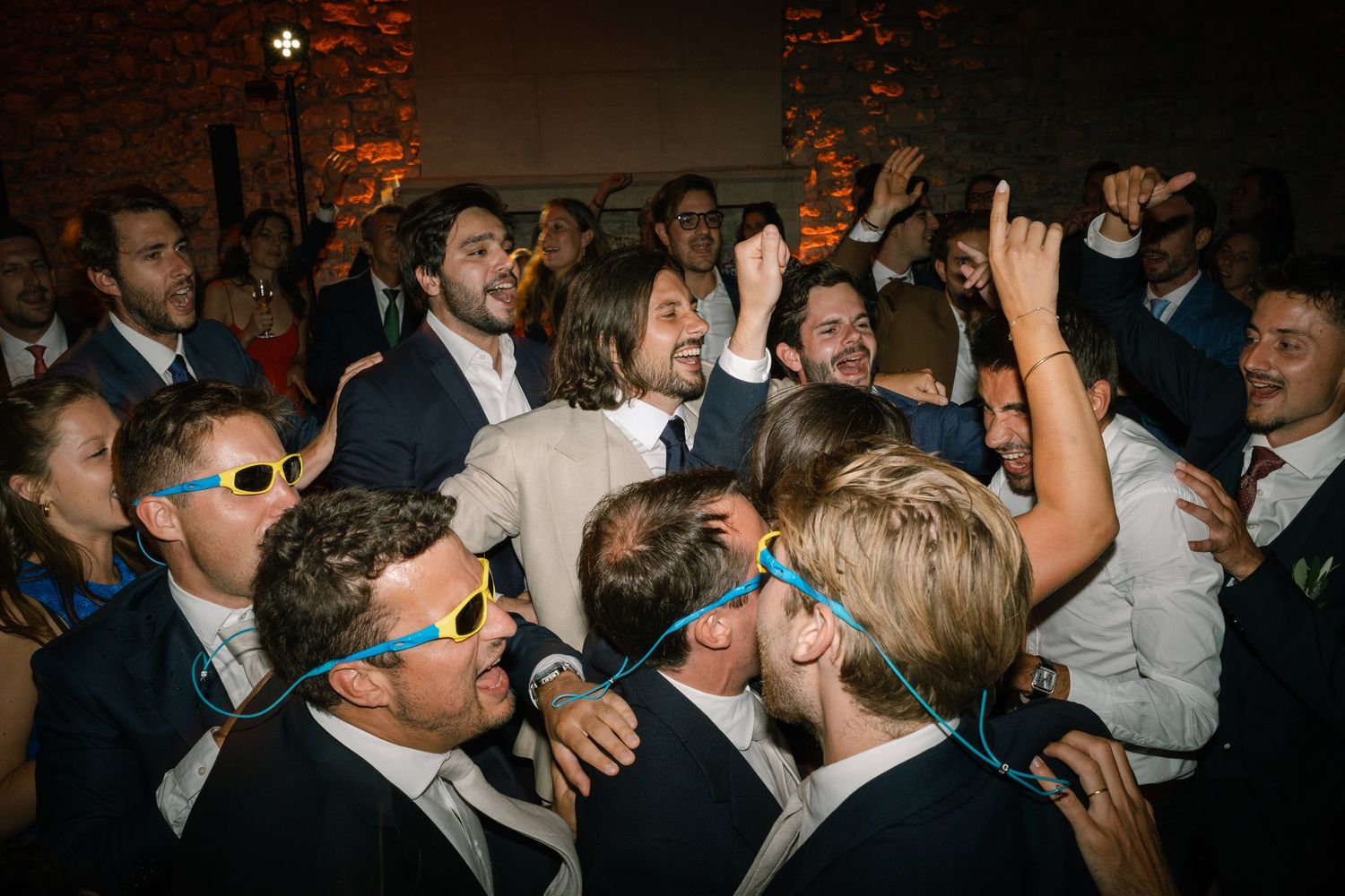 Lively crowd dancing and celebrating at a dimly lit wedding reception.