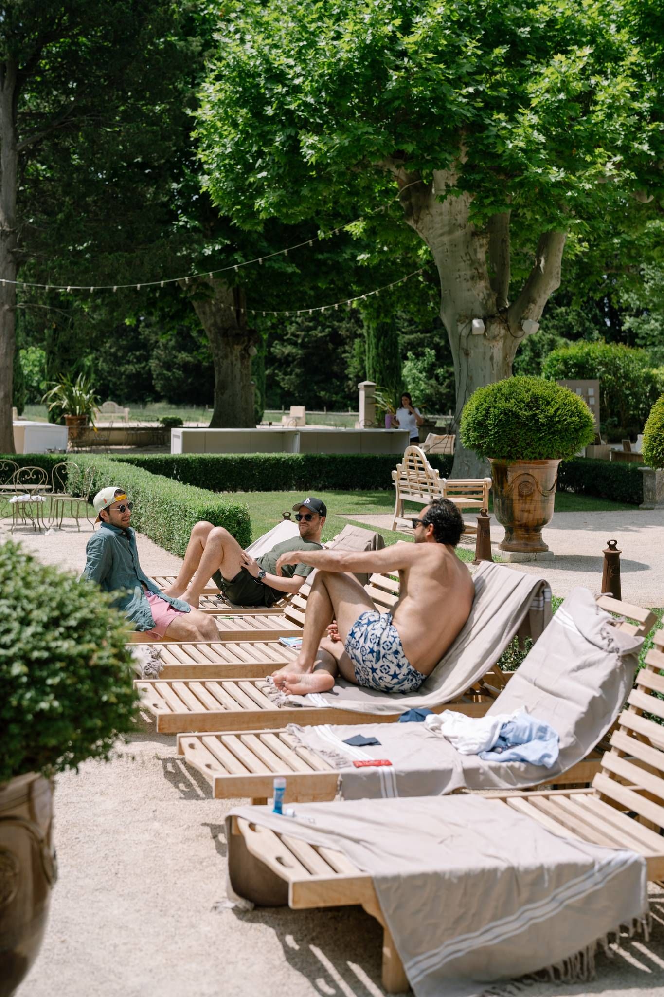 People relaxing on lounge chairs in a peaceful garden setting surrounded by lush green trees.