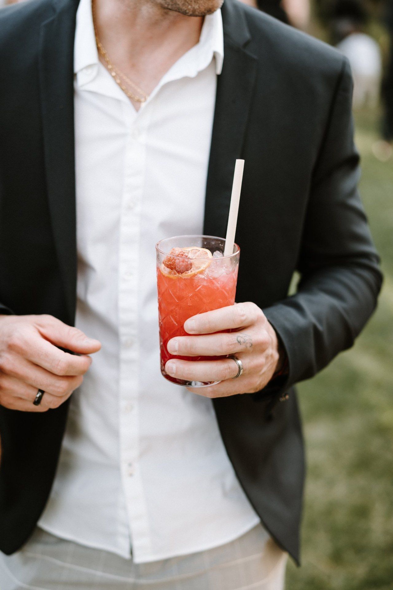 Person in formal attire holding a red cocktail with straw.