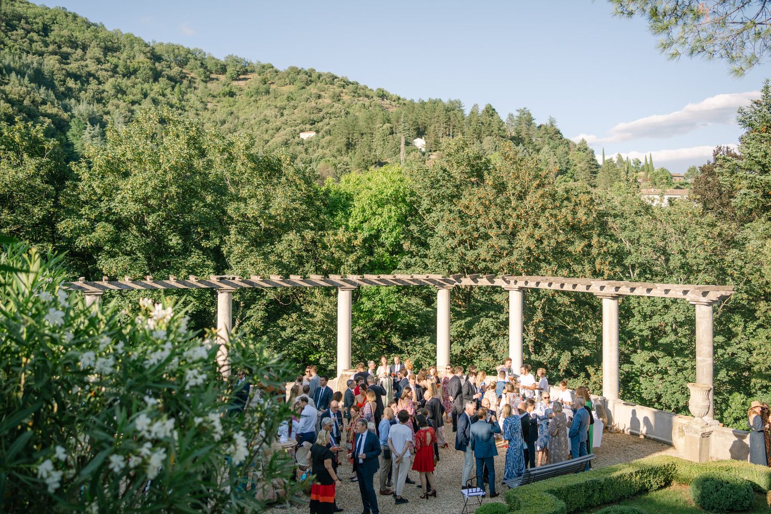 Large group of wedding guests gathered on a scenic terrace surrounded by mountains.