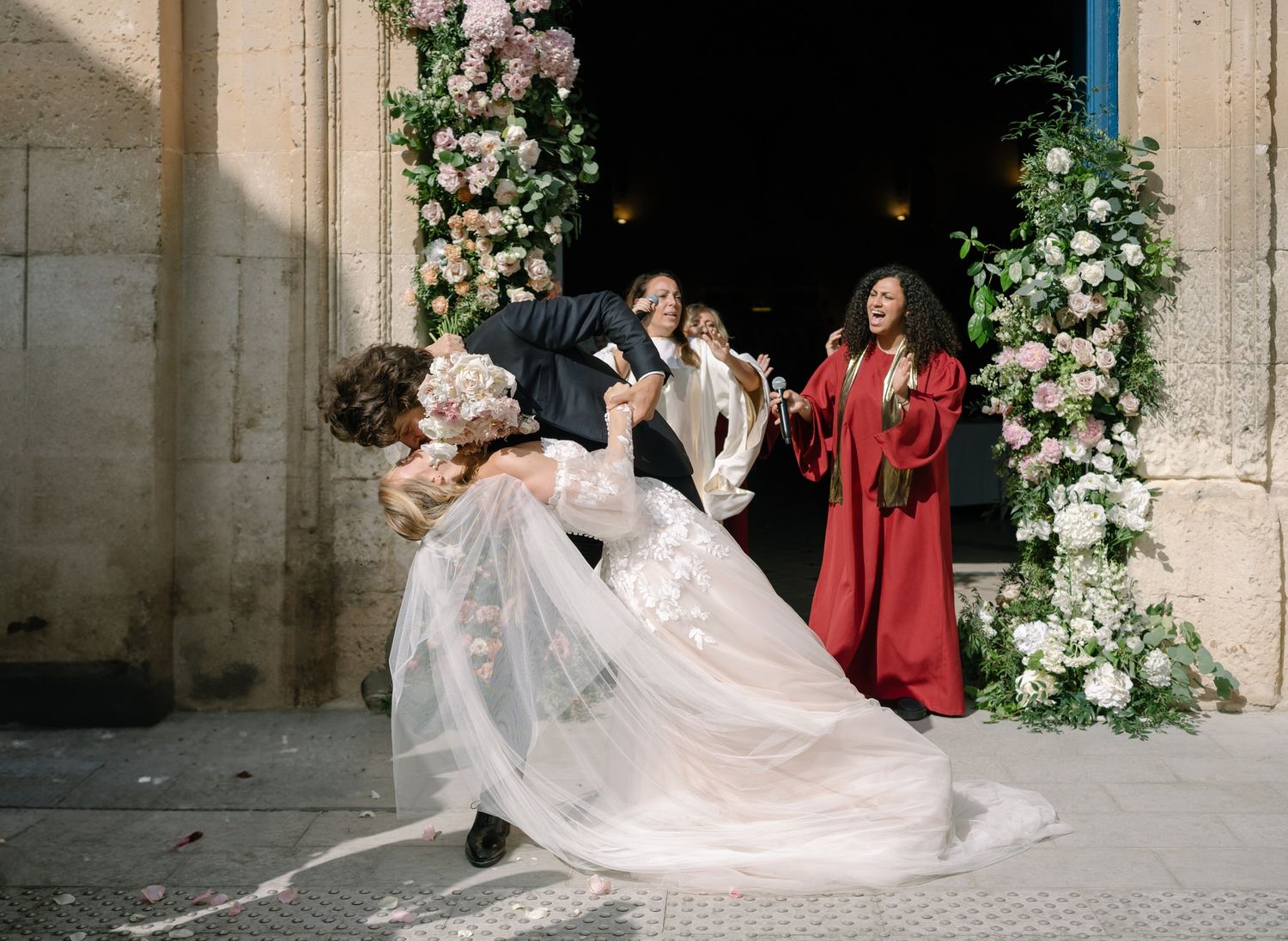 Joyful wedding celebration moment outside historic stone church entrance with floral decorations.