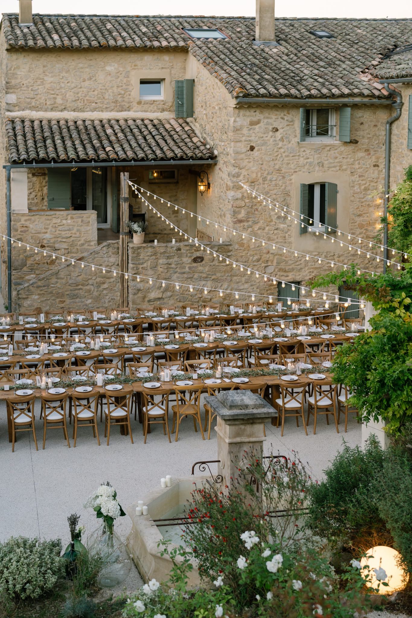 String lights hanging over long wooden tables at an outdoor wedding reception venue.
