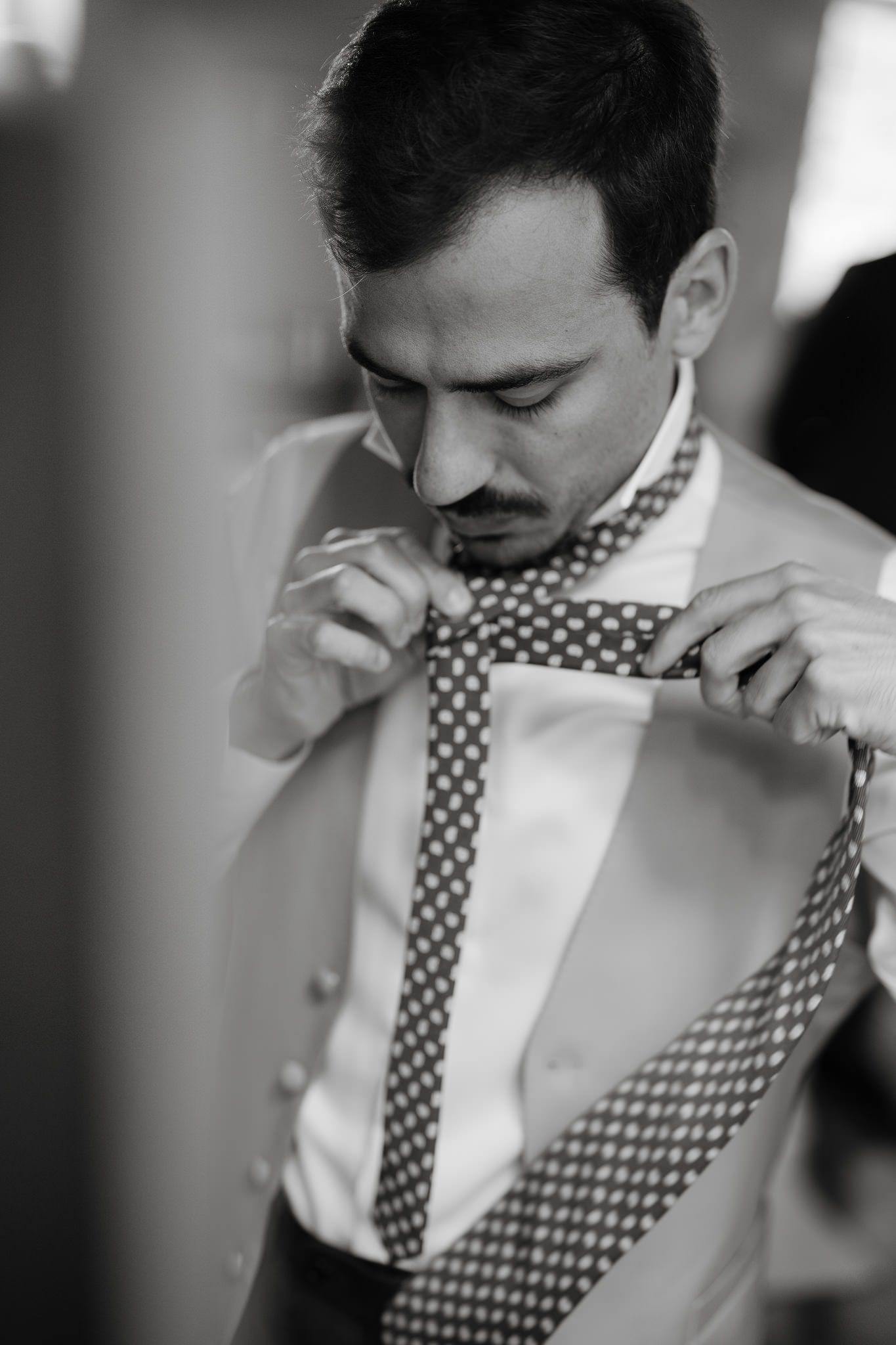Person adjusting a patterned tie while wearing a white dress shirt.