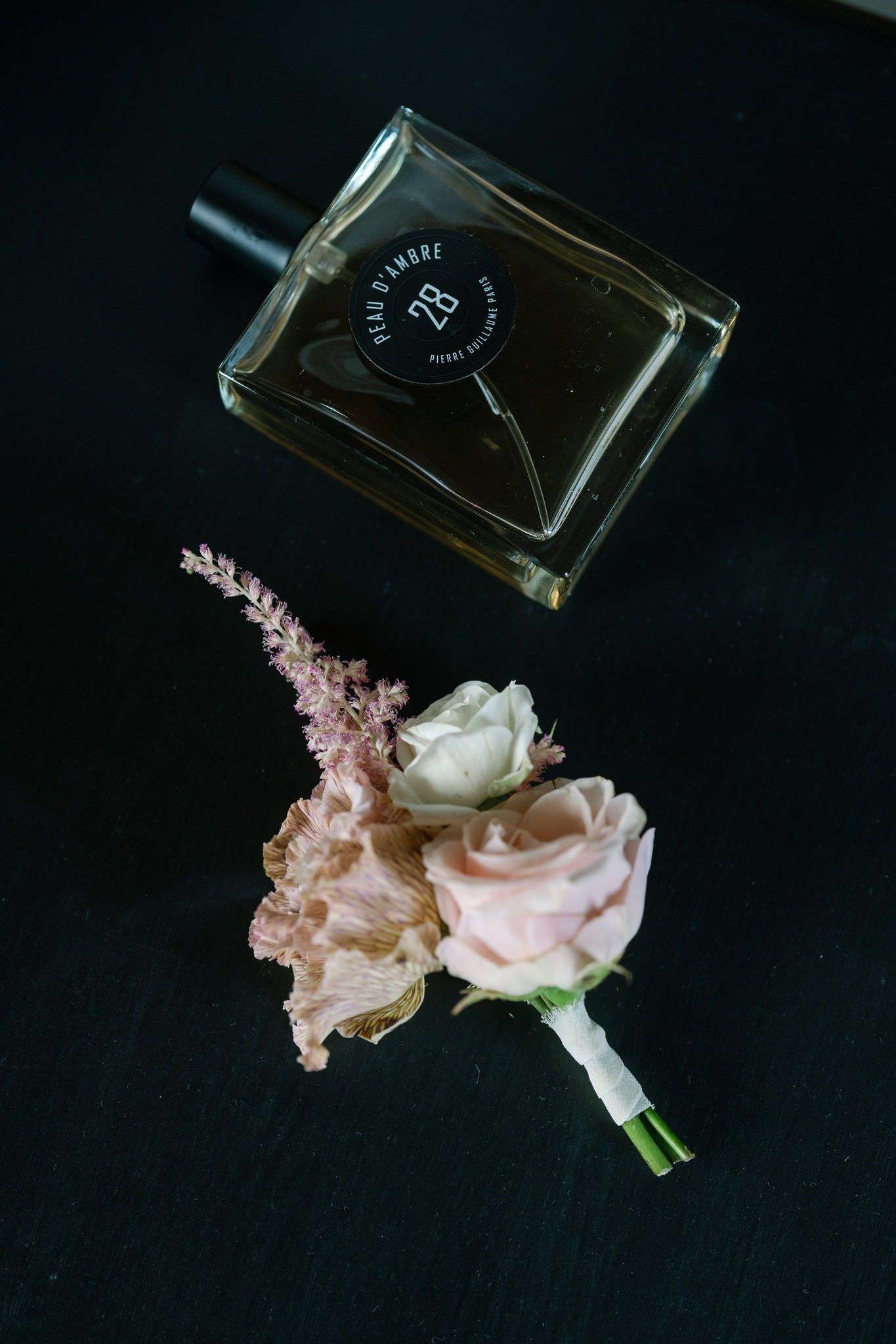 Perfume bottle with delicate pink and white roses against black background.