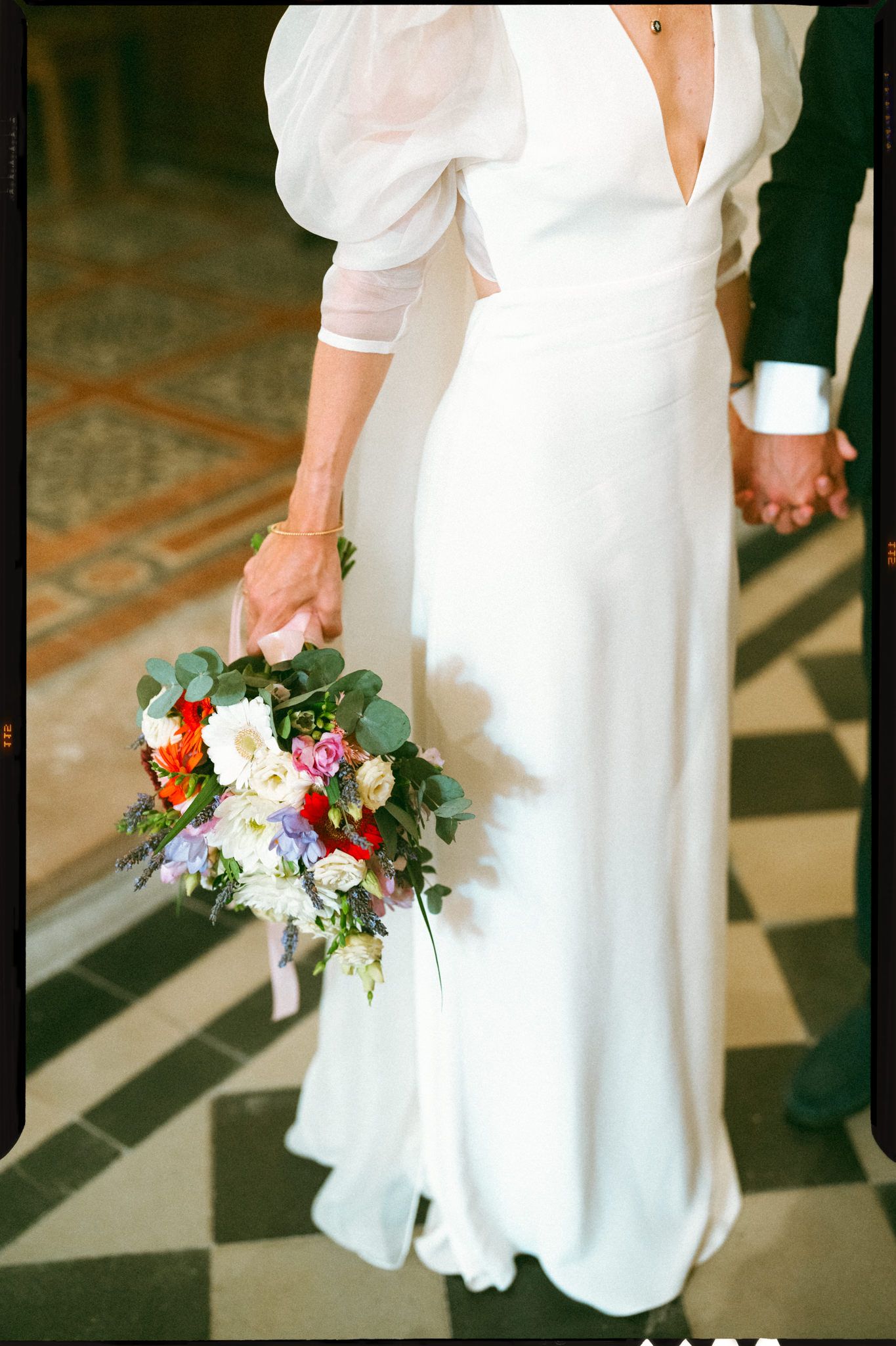 Close-up details of bride's white wedding dress and floral bouquet in sunlit church.