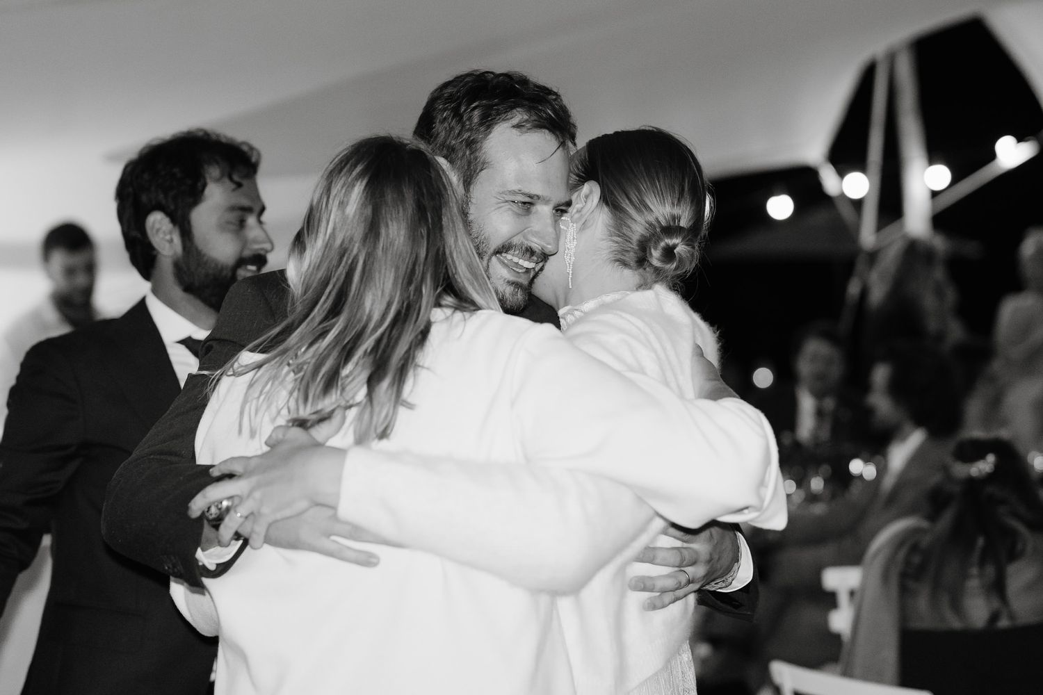 A tender group hug moment captured in black and white during a wedding celebration.