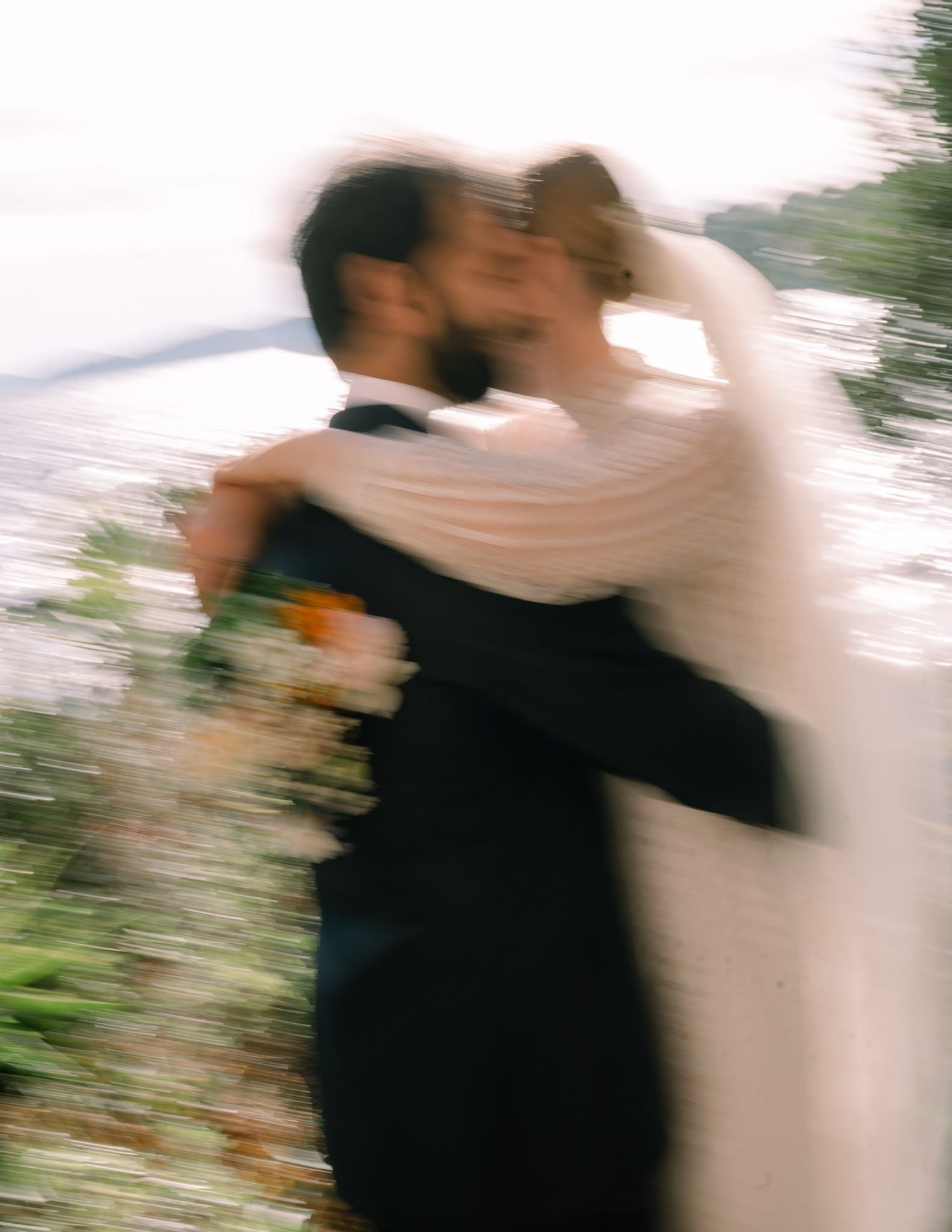 Romantic soft-focus shot of newlyweds embracing outdoors in formal attire.