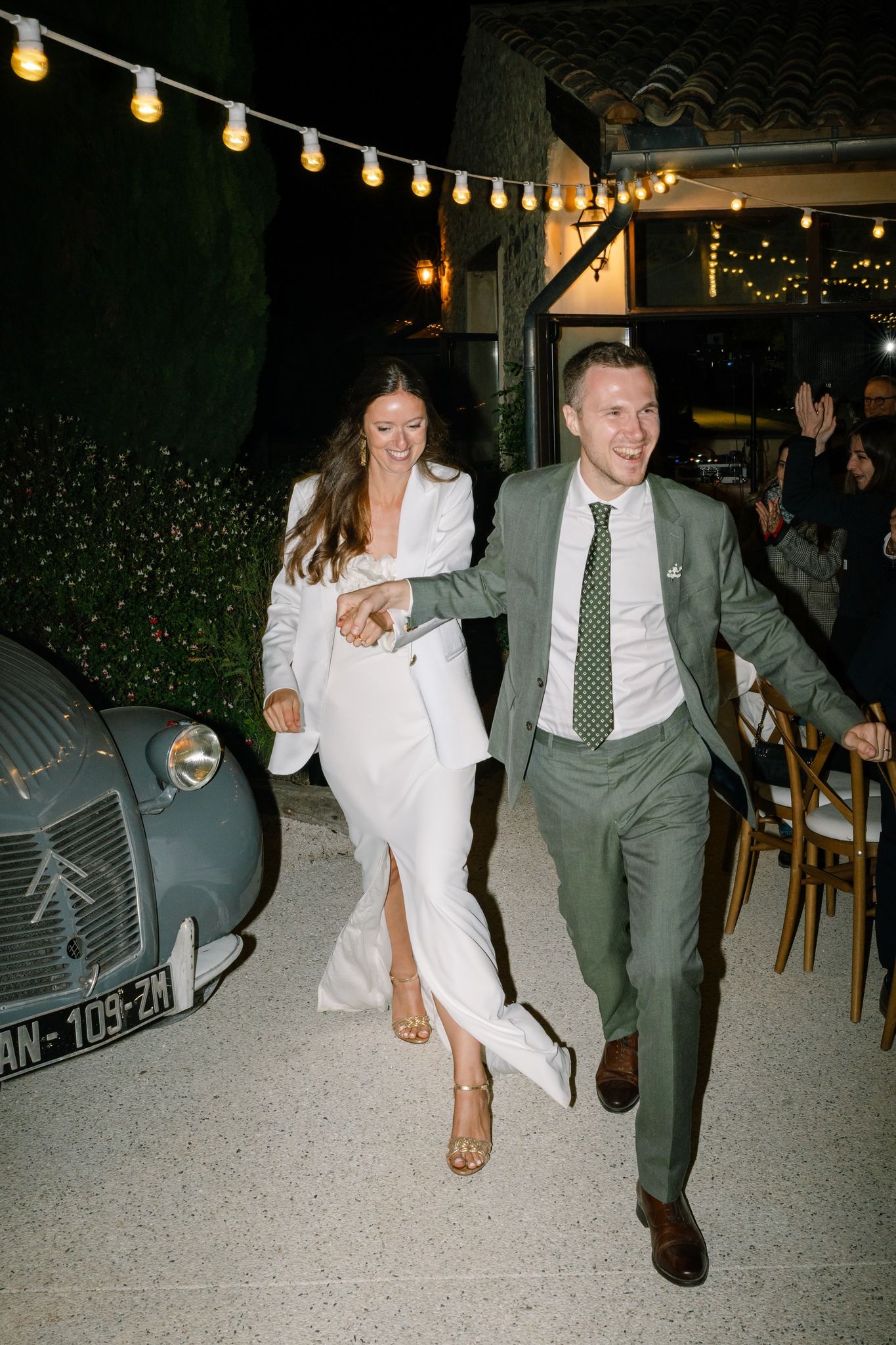 Couple running playfully under string lights at an outdoor evening celebration.
