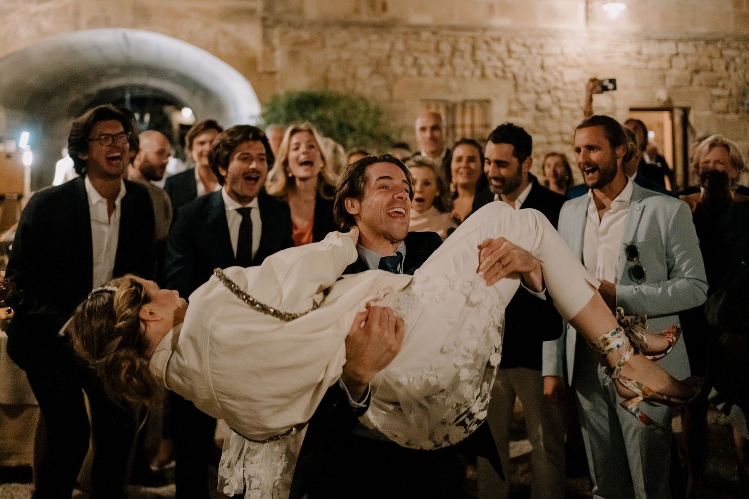 Wedding guests dance and celebrate during an evening reception in a rustic indoor venue.