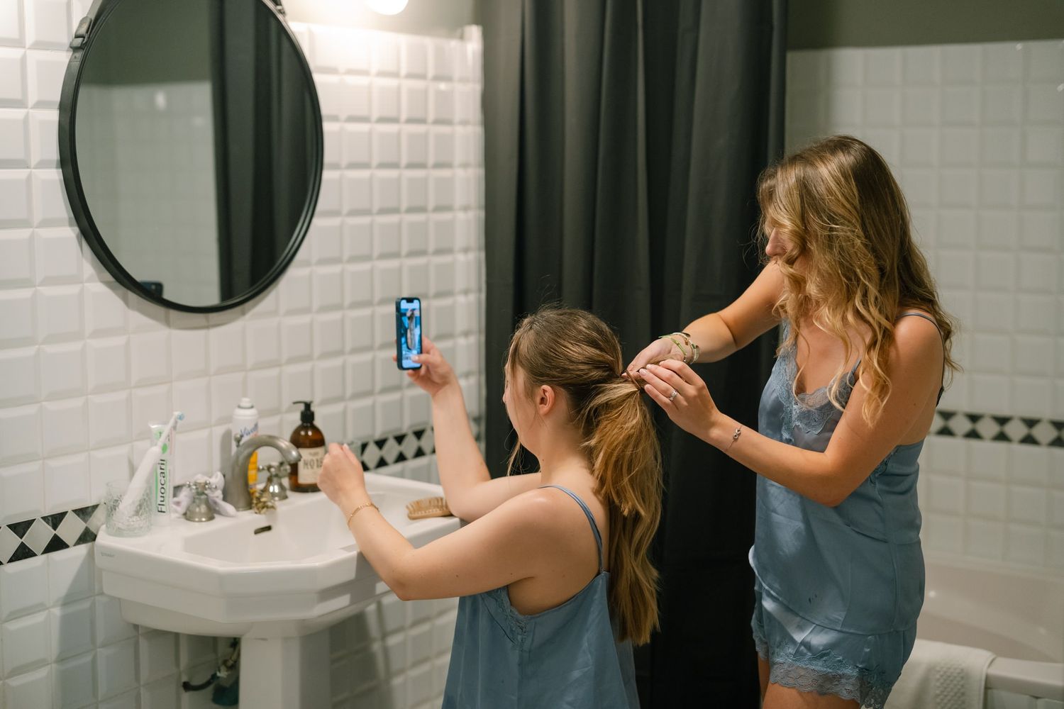 Getting ready in a white tiled bathroom with multiple mirrors and sinks.