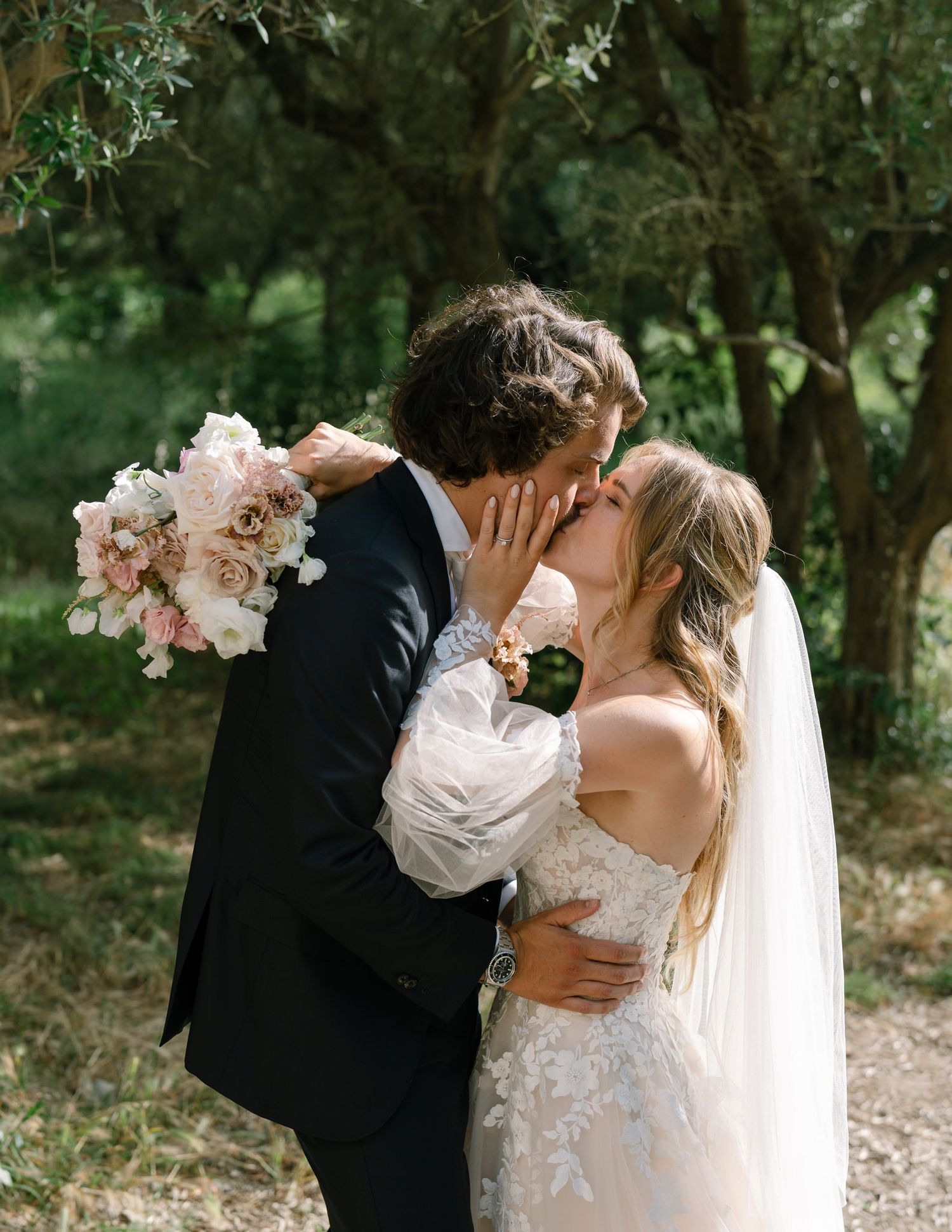 Romantic wedding portrait among olive trees with bride holding pink and white bouquet.