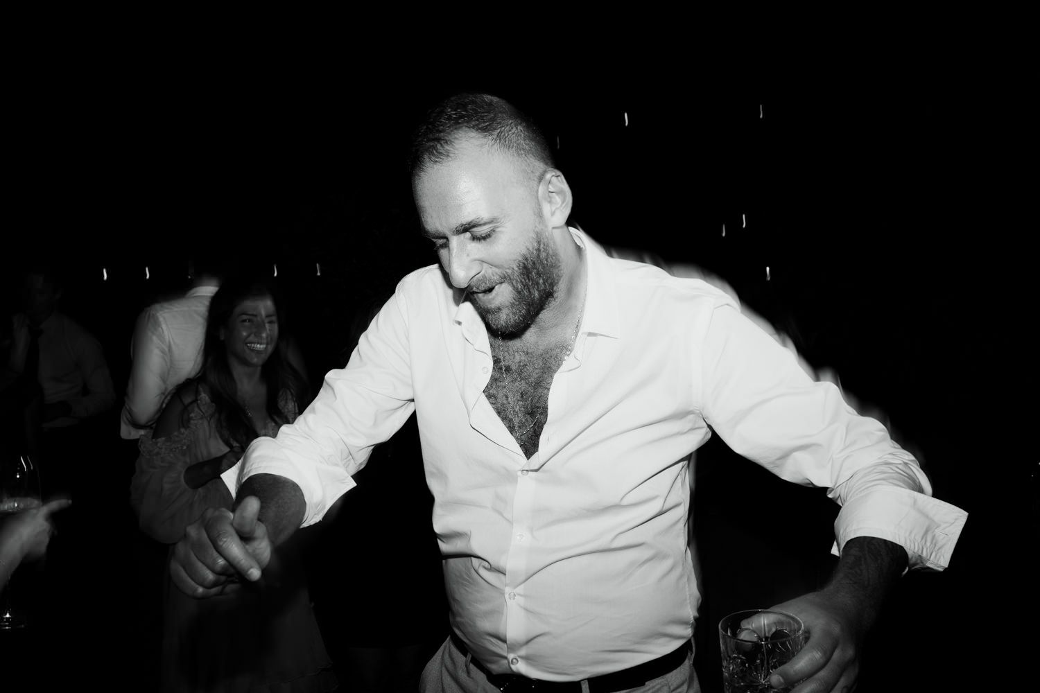 Black and white photo of guests dancing and celebrating at a nighttime event.