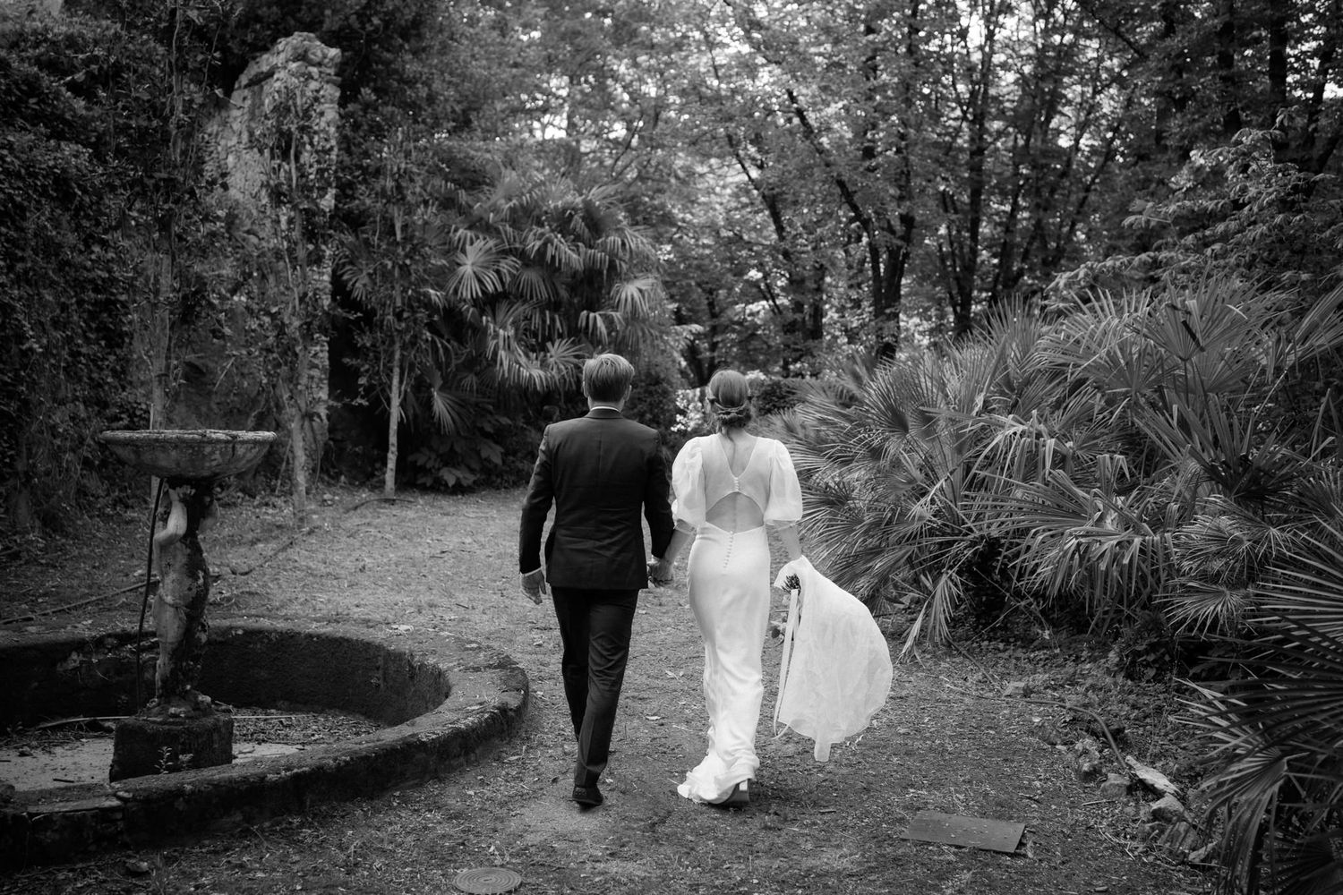 Black and white photo of wedding couple walking through a garden pathway.