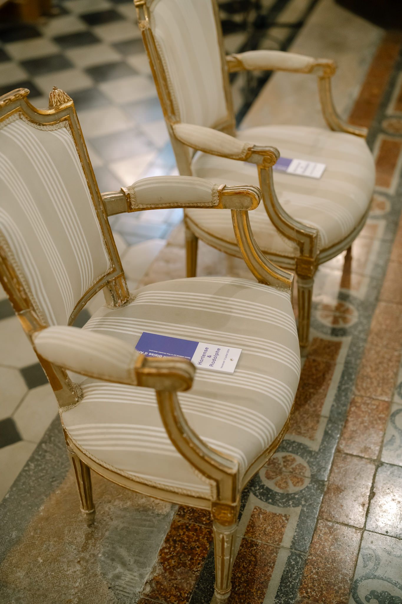 Elegant white upholstered chairs with gold trim and blue programs on seats.
