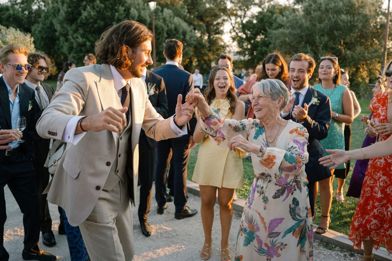 Wedding guests dancing and mingling at an outdoor celebration during sunset.