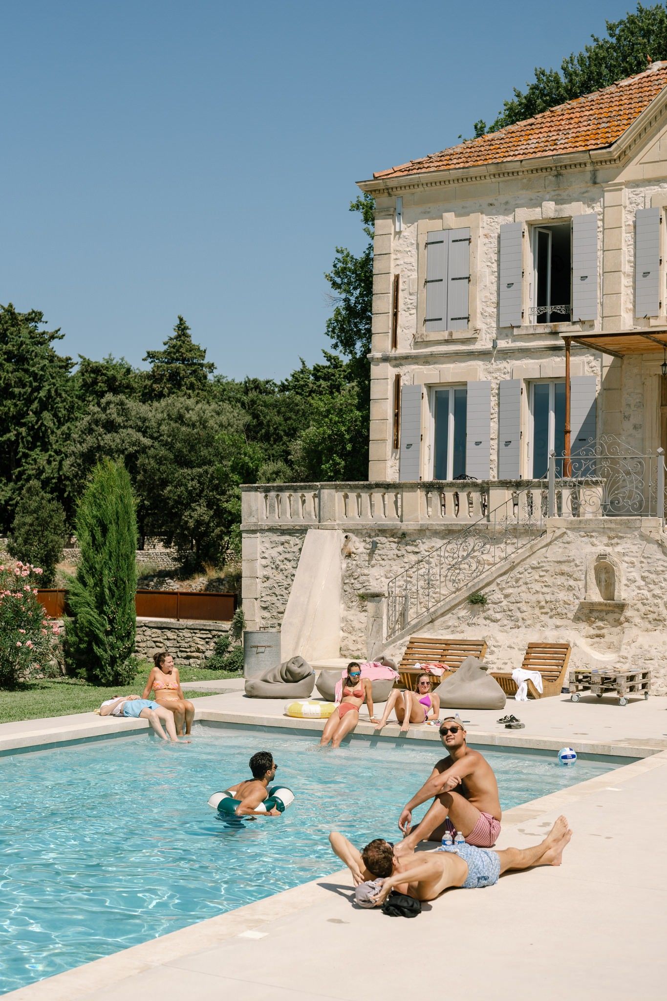 Stone villa with swimming pool where people relax on loungers in summer sunshine.