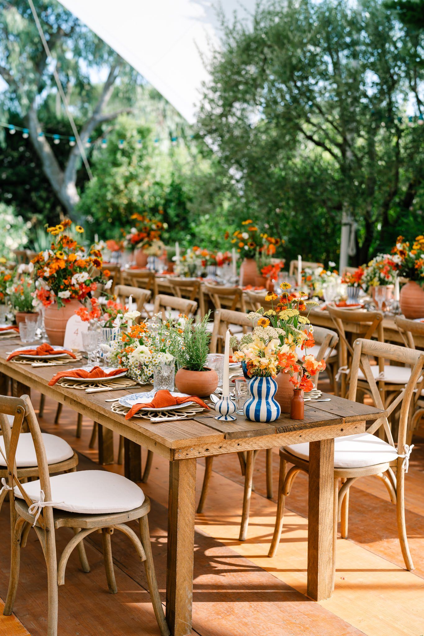 Rustic outdoor dining setup with wooden farm tables and cross-back chairs in a garden setting.