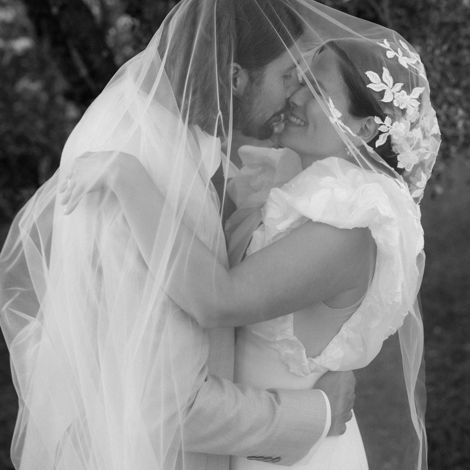 A romantic moment captured through flowing white wedding veil in black and white.