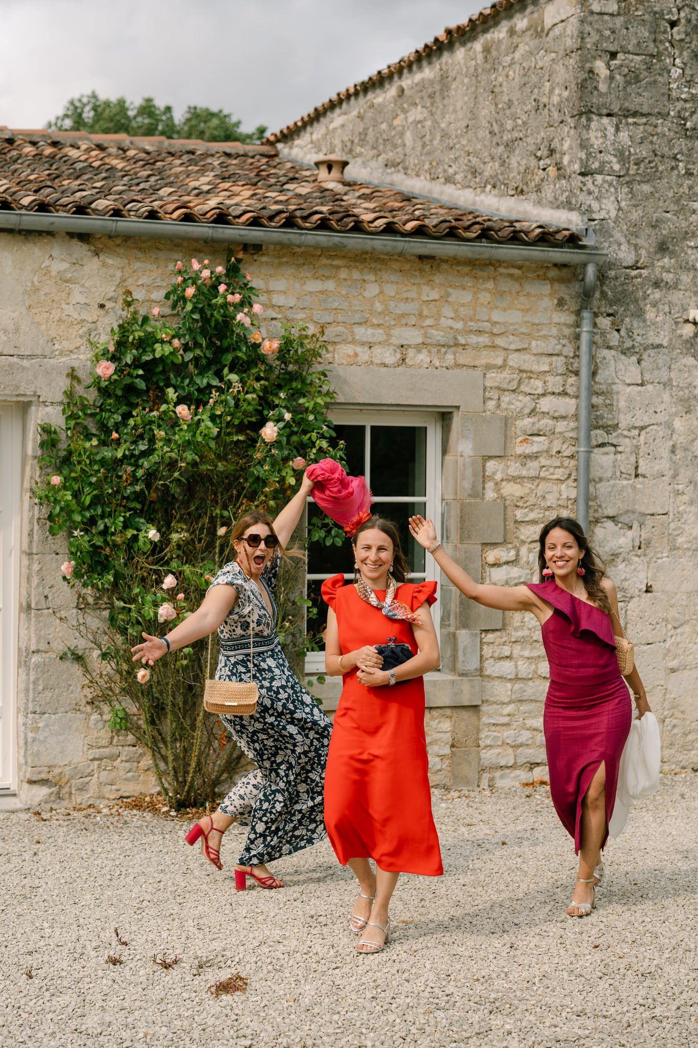 Wedding guests in colorful dresses dancing and celebrating outside a stone building.