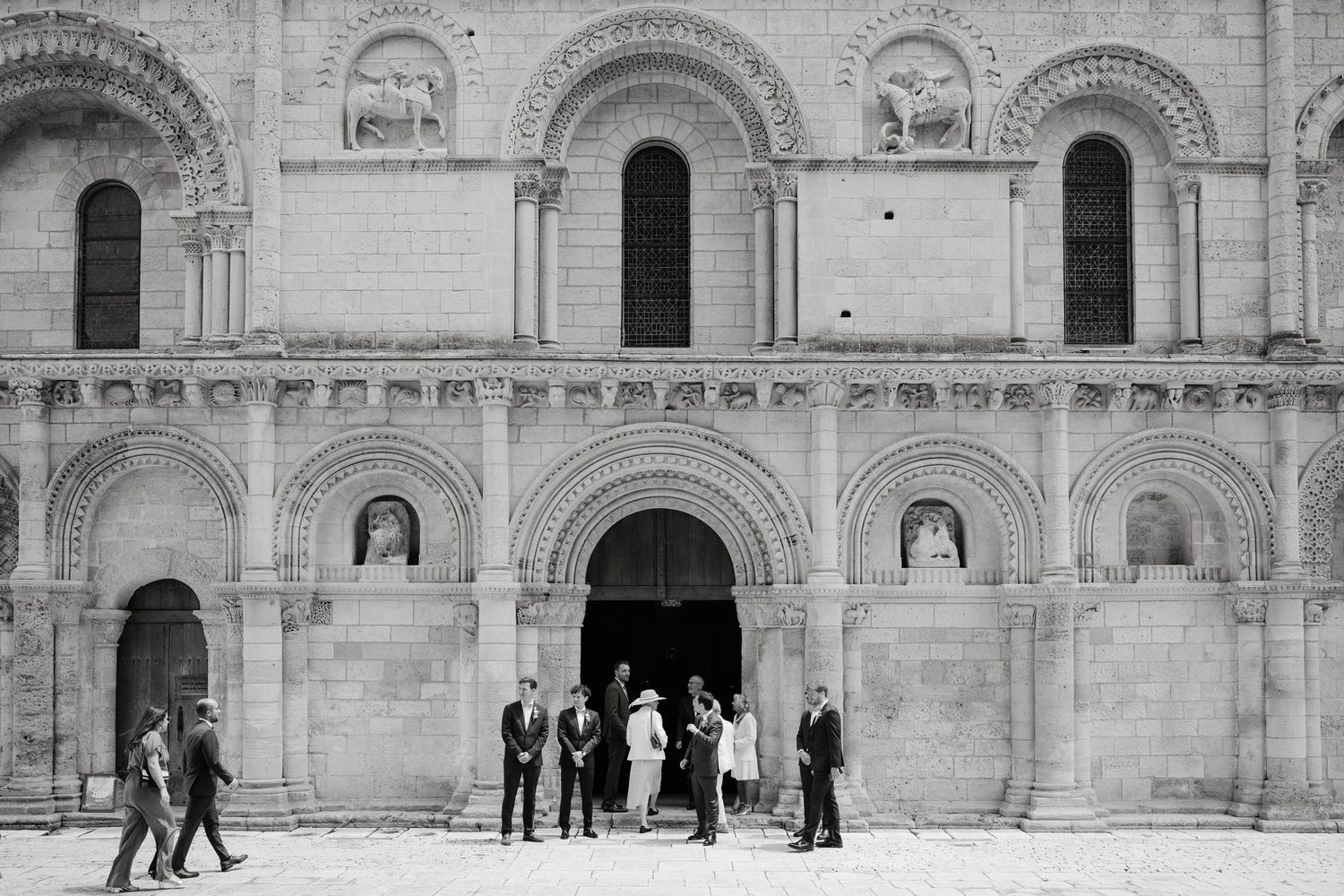 Wedding guests gather outside a historic stone church with arched doorways.